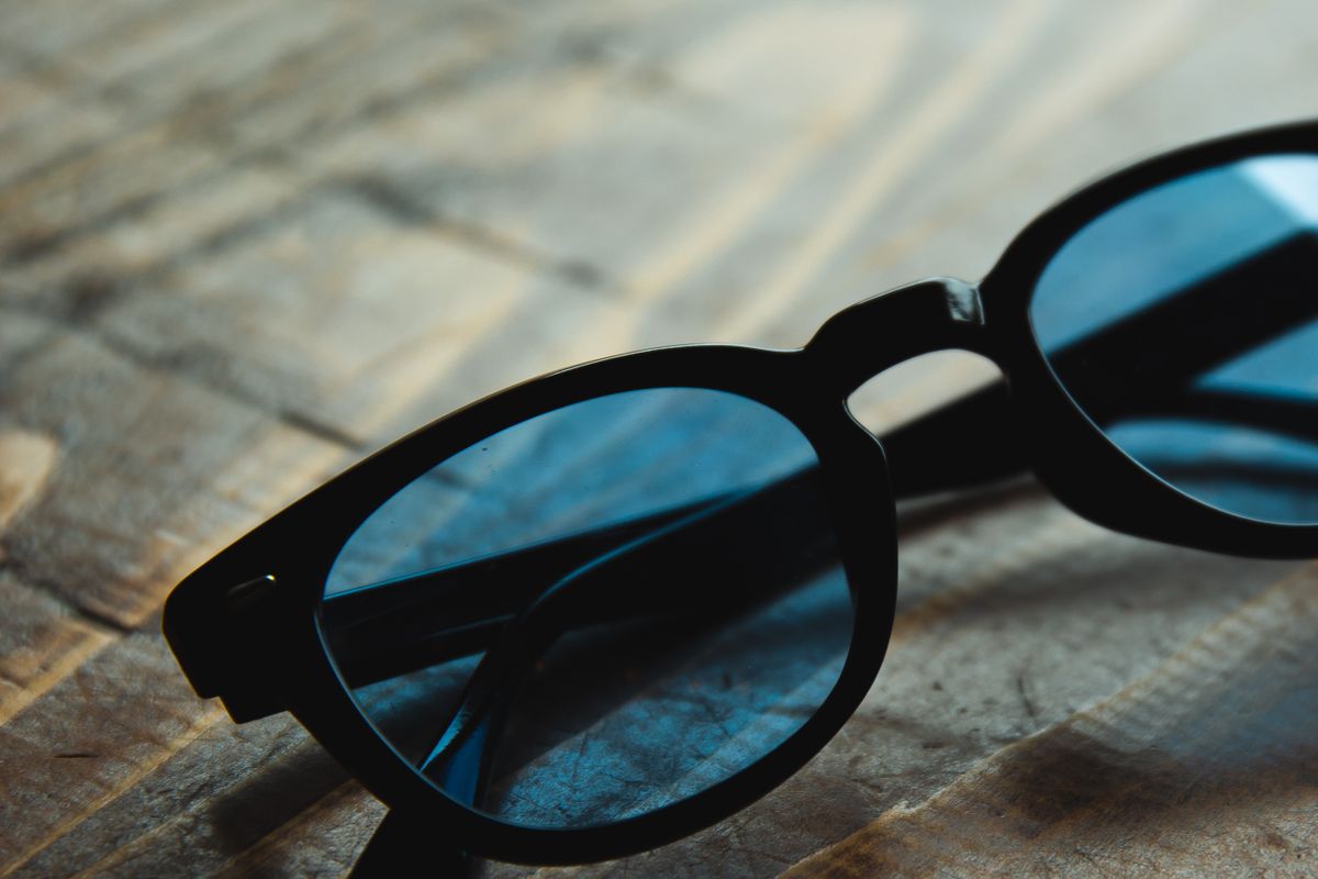 Black-framed sunglasses with blue lenses resting on a wooden surface